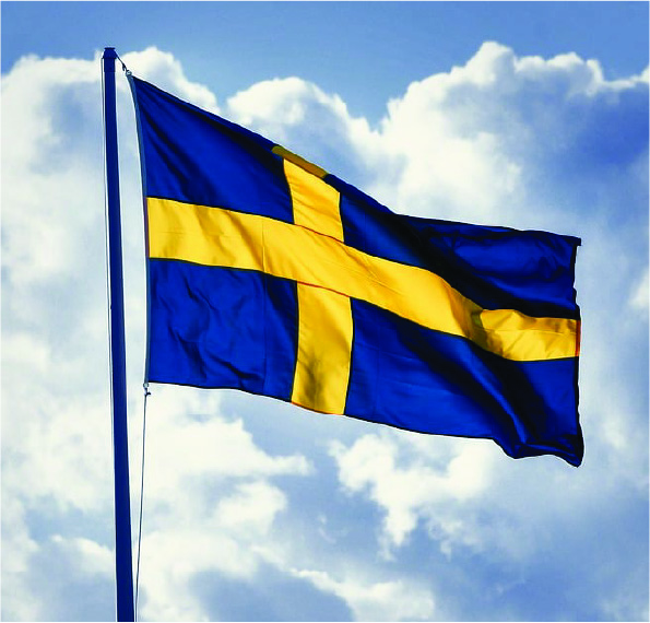 Flaggstång med Svenska flaggan i topp som vajar i vinden mot en blå himmel.