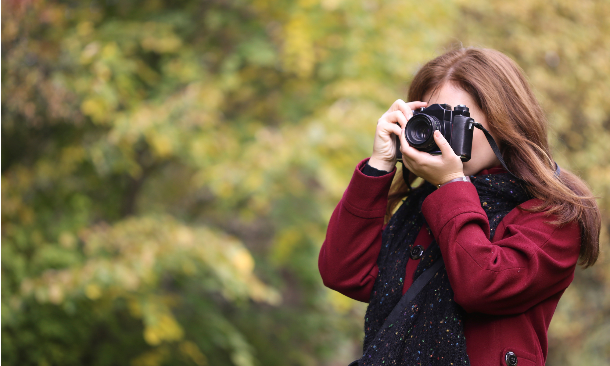 Kvinna med mörkt hår och röd kappa fotograferar i naturskön miljö