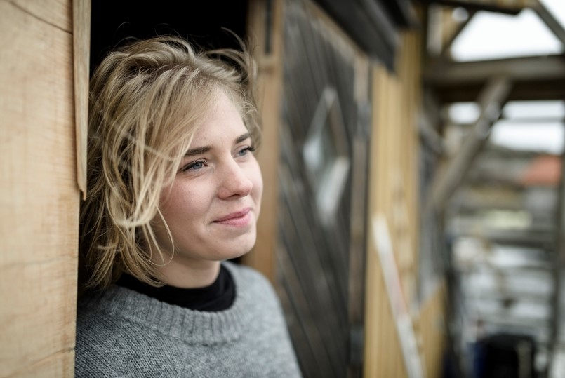 Glad tjej med vinden i håret står vid en ladugårdsvägg