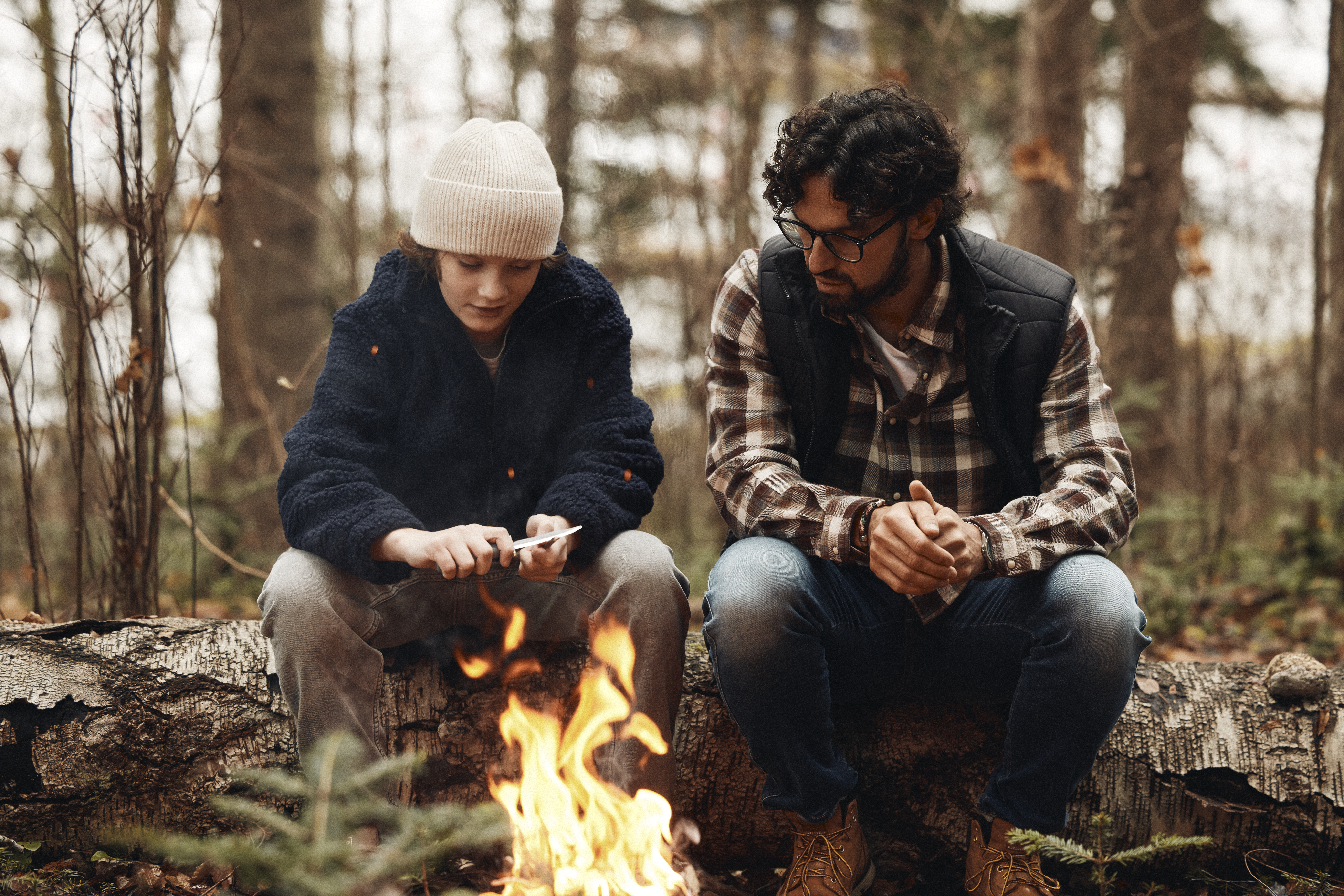 En man sitter  vid en öppen eld tillsammans med en pojke.